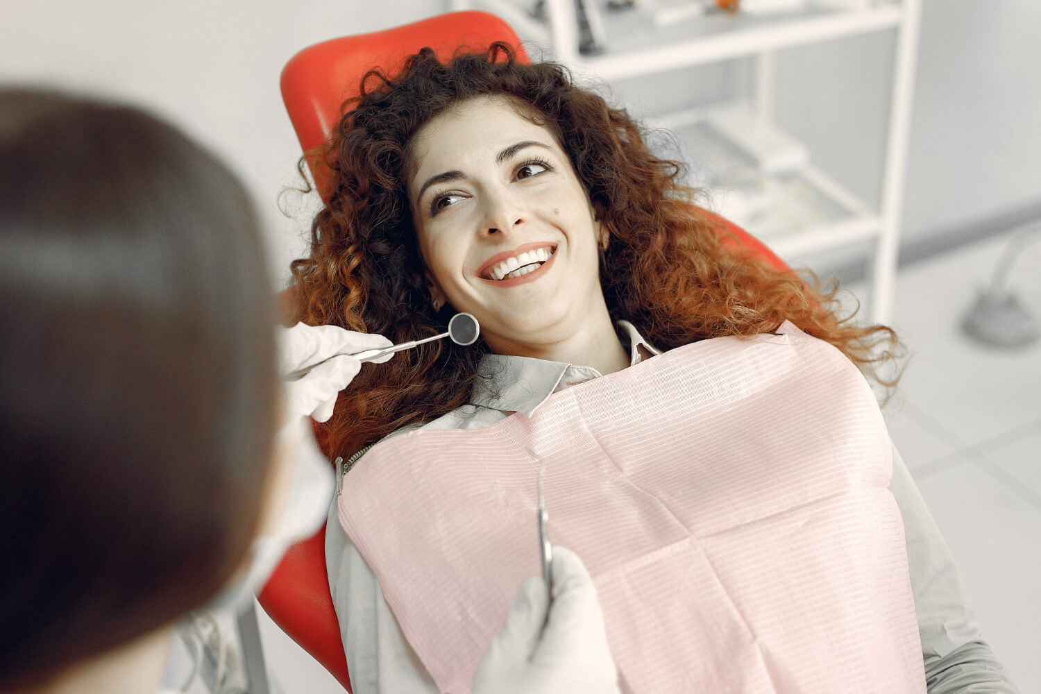 Paciente de cabelos cacheados sorri na cadeira clínica para planejar o uso de lente de contato dental em dente escurecido em Jaguariúna