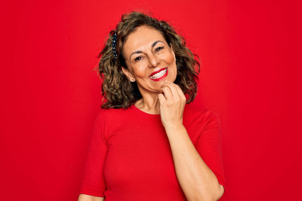 Mulher sorridente com batom vermelho toca o queixo, refletindo a satisfação do implante dentário com carga imediata em Jaguariúna.