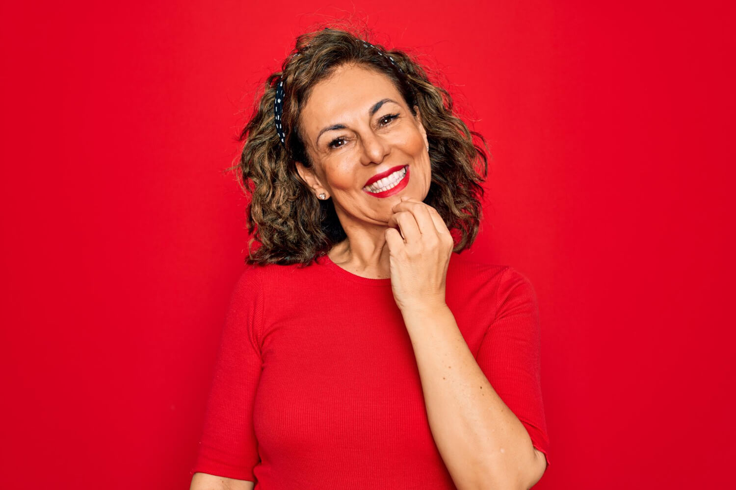 Mulher sorridente com batom vermelho toca o queixo, refletindo a satisfação do implante dentário com carga imediata em Jaguariúna.